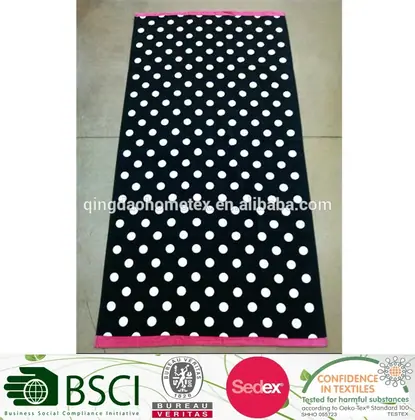 Black beach towel with white polka dots and pink borders laid flat on a tiled floor
