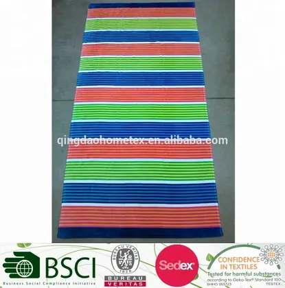 Multicolored striped beach towel in green, blue, coral and orange, laid flat on a gray floor