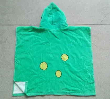 Green hooded terry kids poncho towel with yellow dots, laid flat on grey tiled floor