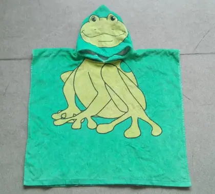 Green hooded kids' bath towel poncho printed with a frog design, laid flat on a grey floor