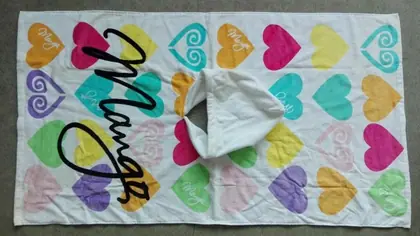 White beach towel with colorful hearts print and large black script lettering, with corner folded over