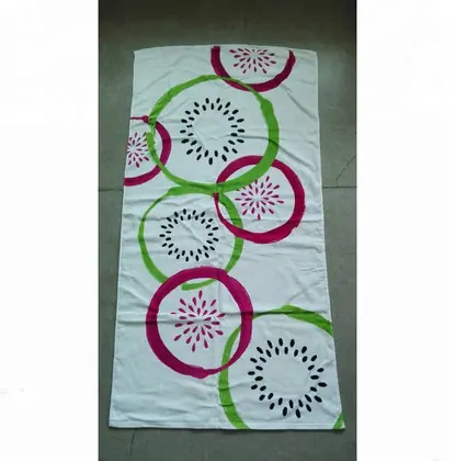 White beach towel printed with pink and green circular patterns and black burst motifs, laid on a tile floor