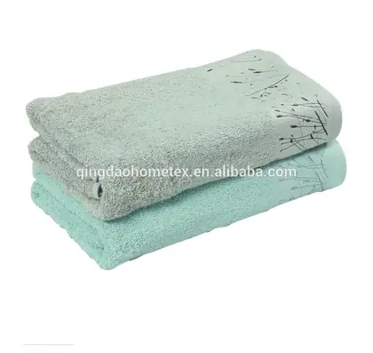 Two folded towels in grey-green and mint tones with a dark botanical print, stacked on a white background.
