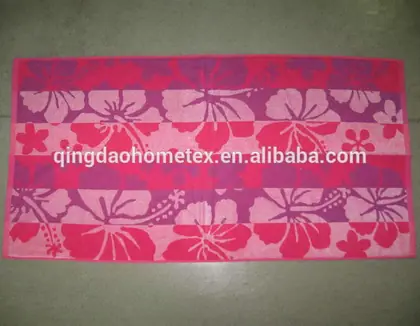Pink and magenta beach towel with hibiscus floral pattern laid flat on a grey floor