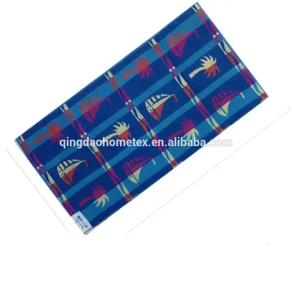 Blue beach towel printed with sailboats and palm trees, displayed diagonally on a white background