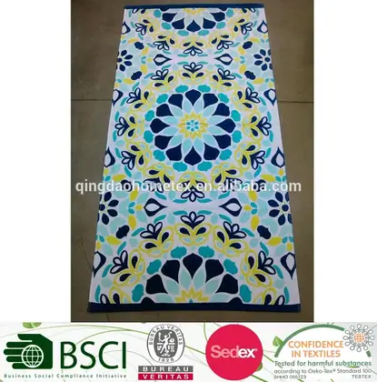 Rectangular beach towel with symmetrical blue, teal and yellow floral print, laid flat on a gray floor