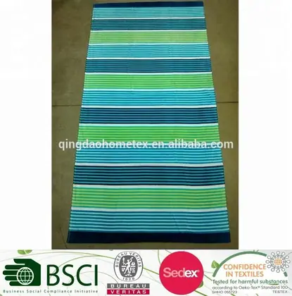 Striped beach towel in green, blue, teal, and white laid flat on a concrete floor