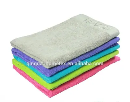 Stack of folded terry towels in beige, purple, teal, green, and pink on a white background