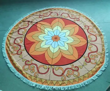Round mandala-printed beach towel with fringe laid flat on a green floor
