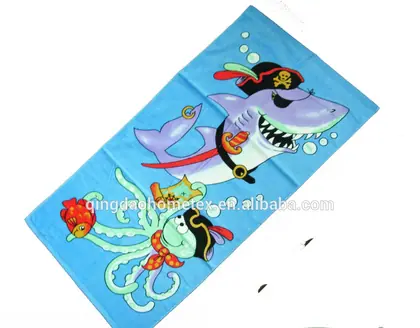 Blue beach towel with pirate shark and octopus cartoon print, shown diagonally with certification logos below