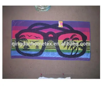 Beach towel printed with sunglasses and tropical palm design, laid flat on a floor