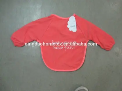Red long-sleeve baby bib with printed text and a tag, lying flat on a gray floor
