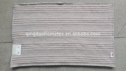 Light gray chenille bath mat with horizontal ribbed texture, laid flat with a small care label attached