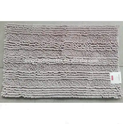 Light beige chenille bath mat with striped textured pile and small tag, on grey floor