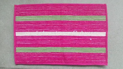Pink woven doormat with green and white stripes photographed flat on a gray surface