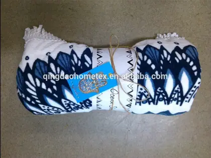 Rolled white blanket with navy blue ikat-style print, fringe ends, tied with string and a blue tag