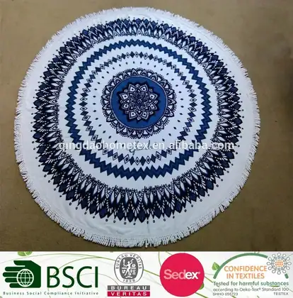 Round white beach towel with blue mandala pattern and fringe, laid flat, with certification logos below