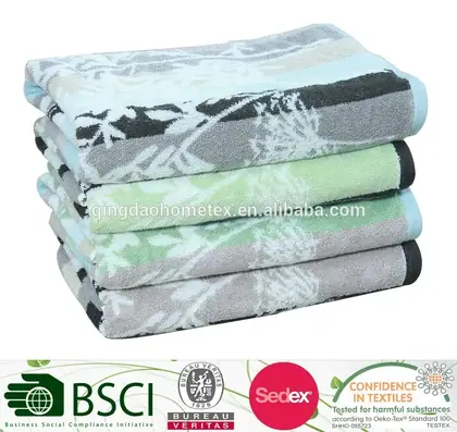 Stack of folded yarn-dyed towels with floral leaf patterns in grey, black, blue and green on a white background.