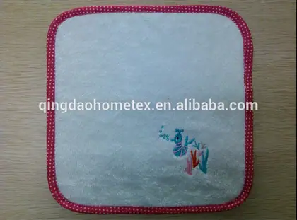 White square towel with pink polka-dot trim and small embroidered marine design, on a wooden surface