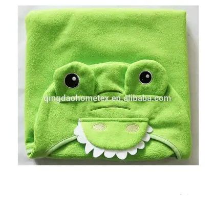 Green frog-shaped hooded baby towel folded flat with embroidered eyes and teeth on white background