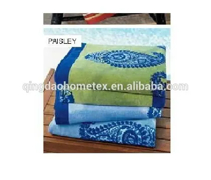 Folded paisley-patterned beach towels in green and blue stacked on a wooden surface near a pool