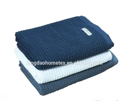 Stack of folded waffle-weave towels in navy, white, and gray-blue with certification logos below