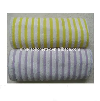 Two rolled striped terry towels, one yellow and white and one purple and white, on a textured surface