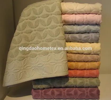 Stack of folded cotton towels in assorted pastel colors with floral jacquard weave, one towel draped in front