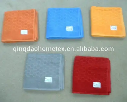 Five folded textured towels in orange, blue, yellow, grey and red laid on a beige carpet