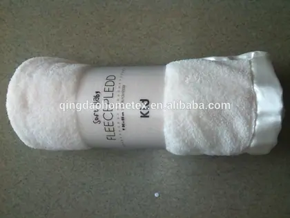 Rolled white baby blanket with white satin trim and printed paper packaging band on a grey surface