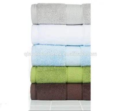 Stack of folded terry towels in grey, white, light blue, green, and brown on a white tiled surface