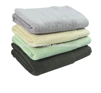 Stack of four folded terry towels in grey, cream, green and dark charcoal on a white background
