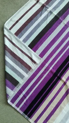 Folded striped towel in purple, black, white and maroon stripes lying on a gray surface