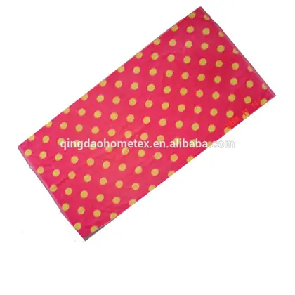 Red beach towel with yellow polka dots laid flat on a white background