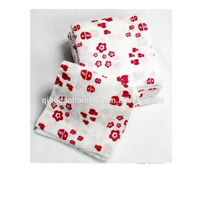 Stack of folded white muslin cloths printed with red ladybugs and flowers