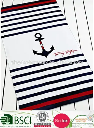 Navy, white and red striped beach towel with black anchor print and red script lettering, shown flat on a white slatted surface
