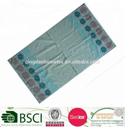 Pale green beach towel with blue and pink floral corner patterns, shown diagonally with certification logos below