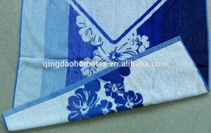 Folded white and blue towels with floral jacquard pattern stacked on a plain surface