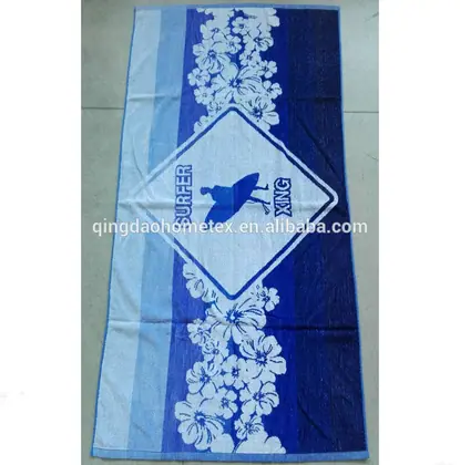 Blue and white floral beach towel with a surfer graphic and 'SURFER' text, photographed flat on a tiled floor