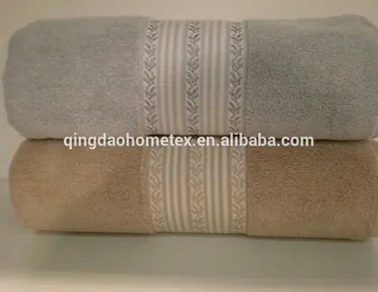 Two folded towels, gray and beige, with striped leaf-pattern bands, stacked on a white surface