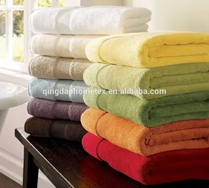 Stacks of folded bath towels in assorted colors on a dark table beside a bright window