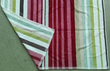 Multicolored striped towel with one corner folded over, laid flat on a green fabric surface