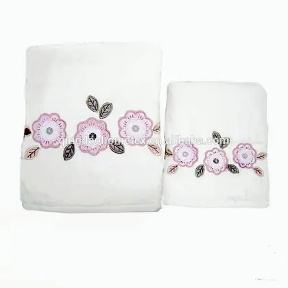 Two white folded towels with pink flower applique and leaf embroidery on a white background