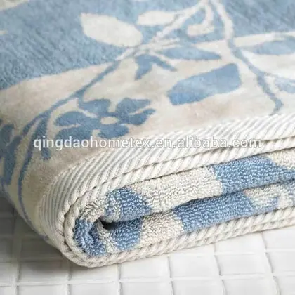 Close-up of a folded blue and white floral jacquard towel on a white tiled surface