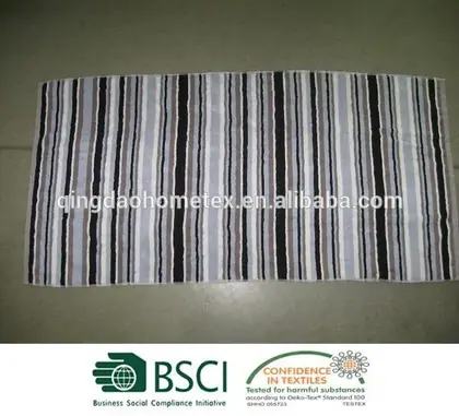 Striped towel in black, gray, and white vertical stripes laid flat on a dark tiled floor