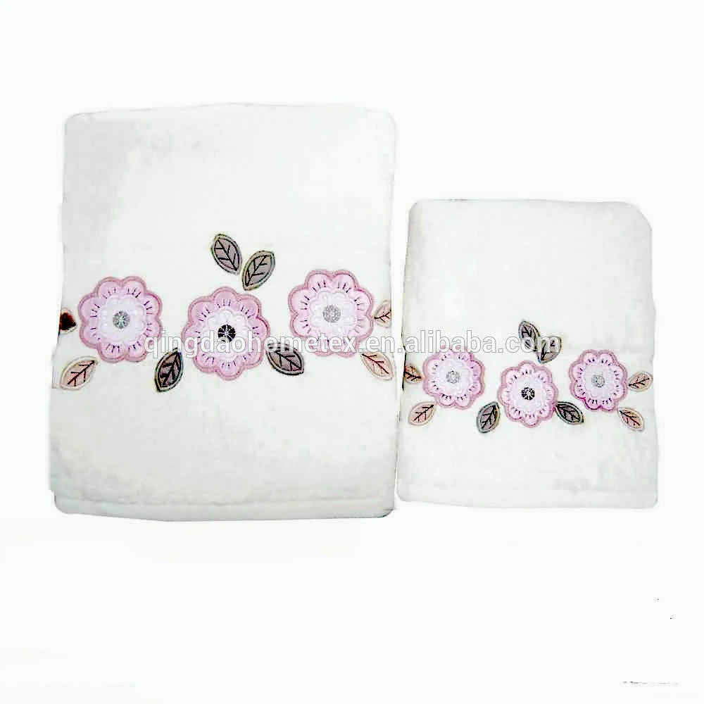 Two white folded towels with pink flower applique and leaf embroidery on a white background