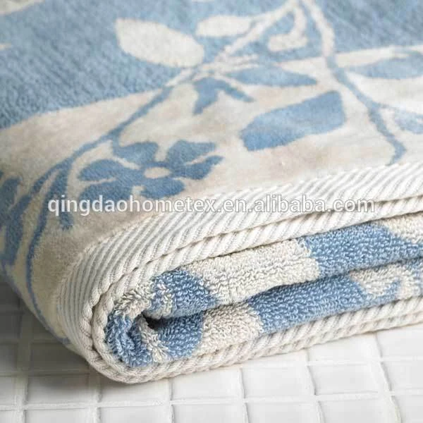 Close-up of a folded blue and white floral jacquard towel on a white tiled surface