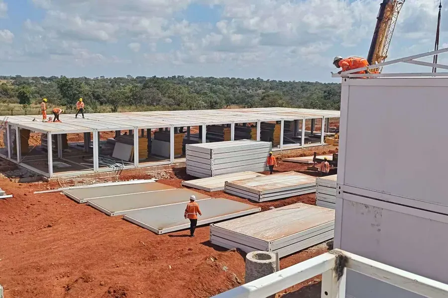 Workforce camp under construction with stacked wall panels and a crane in Guinea