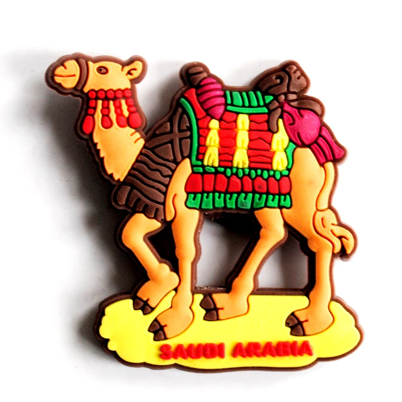 Soft PVC magnet of a walking camel with a green and red decorated saddle and tassels on a yellow base