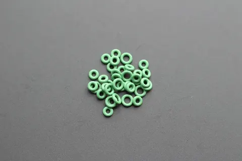 Cluster of small green FFKM O-rings on a grey studio surface